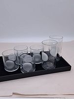 Set of six vintage clear glasses with white circular design placed on a black tray, two taller glasses and four shorter glasses visible.