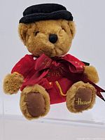 Full front view of the vintage Harrods bear wearing a red jacket, black hat, and bow.