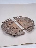 Top view of the expandable silverplate trivet in closed position showing detailed cut-out floral and abstract patterns with tarnish and wear