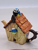 Photo of the teapot from an angled side view showing the birdhouse shape, roof, and spout