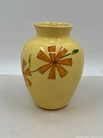 Front view of a yellow glazed ceramic vase with orange flowers and green stems painted on the surface, showing the oval shape and wide mouth.