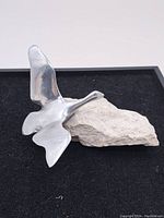 Aluminum swan sculpture mounted on natural stone base, shown from a side angle to highlight shape and form.