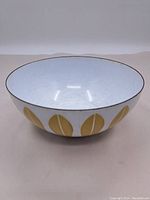 Front view of enamel bowl showing round shape, white interior with surface scratches, and yellow leaf motifs on exterior.