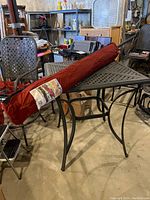 Full view of Hampton Bay red umbrella in original carrying sleeve placed on black metal table.