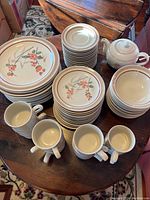 Photo showing stacks of various plates, bowls and coffee cups along with one teapot placed on a wooden table.