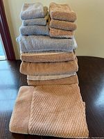 Photo shows a neatly stacked set of beige and gray bath towels, washcloths, and a beige textured bath mat arranged on a table.