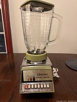 Front view of Osterizer Pulsematic blender with glass jar on a wooden table, showing the control panel with multiple buttons and brand name.
