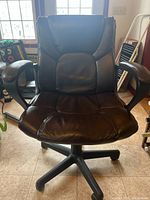 Front view of the dark brown simulated leather office chair showing padded seat, backrest and armrests, five black caster base.