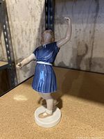 Photo of ballerina figurine from side angle showing blue dress, one arm raised and round base.