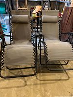 Front view of two beige folding chaise lounge chairs with dark brown frames, beige fabric, and neck pillows.