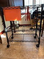 Front and side view of one black metal rolling file cart with four casters, two locking, with orange hanging dividers and wire shelves.