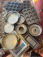 Overview of entire variety of metal bakeware laid out, showing muffin pans, bundt pan, springform pan, cake pans, cookie sheets, and molds