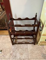 Front view of dark stained wooden wine rack with four tiers for holding wine bottles, decorative metal finials on the four vertical posts.
