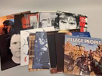 Thirteen vinyl records arranged in a pile showing front album covers including U2, Village People, Phil Collins, Spandau Ballet, and The Alan Parsons Project.