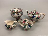 All four porcelain pieces arranged together showing flower frog vase, teapot, sugar bowl, and creamer