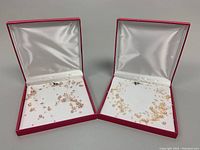 Two pearl garland choker necklaces displayed in open red jewelry boxes with satin lining, showing packaging and presentation.