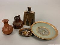 Five pottery pieces arrayed together including a plate, two pitchers, a bottle, and a small dish.