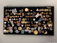 Full overview of over 60 assorted vintage pins displayed on black board