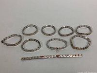 Nine vintage Italian link stretch charm bracelets arranged in a semi-circle with one bracelet extended horizontally. The bracelets are made from square metal links, some with gold-tone decorative elements.