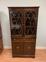 Front view of wooden corner display cabinet with glass doors and lattice design, lower drawer and cupboard storage.