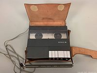 UHER 4000 Report-L tape recorder powered off inside a leather case, front left view showing power cord and case details.