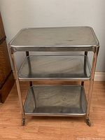 Front view showing the three stainless steel shelves and caster wheels on the cart.