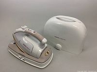 Front right view of cordless steam iron on charging base with white cover case behind