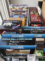 Various baseball collectibles packed together including acrylic ball and card holders, a baseball glove display case, a MLB card collector's tin, and a boxed display case.