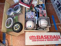 Box of 1989 Fleer Baseball cards and assorted sports collectibles including two displayed baseballs, hockey pucks, and trading cards.