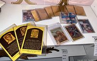 Display of baseball-related collectibles including embossed golden plaque Hall of Fame postcards, MLB bubble gum cards in holders, and a Ted Williams 1938 card.