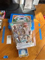 Bratz doll in original packaging with winter accessories, Thomas the Train collectible tin box in background, and stack of photo trading cards in front