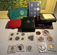 Wide shot showing multiple coin sets in folders and cases alongside loose coins, medallions, and a green cloth bag.