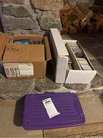 Two cardboard storage boxes filled with trading cards, one purple bin underneath
