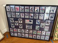 Full view of the framed Patriots football cards collection with 40x32 inch frame on a wooden floor, showing cards and team logo.