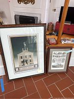 Two framed architectural prints leaning against a wall. Larger frame shows Custom House building, smaller frame shows multiple architectural sketches.