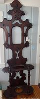 Full view of the antique hall tree, showing overall shape, hooks, umbrella stand base and carved details.