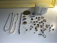 Full lot with necklaces, rings, earrings, pendants, brooches, and jewelry box in white textured case