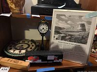 Shelf showing the miniature Shepherd clock, framed railroad advertisement, Lionel model train boxcar, and Lionel wall clock