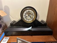 Front view of black slate mantel clock on wooden surface.