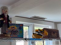 Shelf showing Alexander Graham Bell figure, M&M's candy dish telephone in original box, and wooden trinket box.