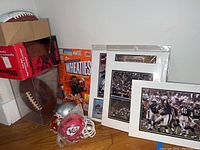 Overview of lot with signed football in a display case, mini helmets including a Chiefs helmet, and three framed photos leaning against wall