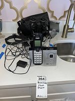 VTech cordless phone and Russian binoculars with case on a kitchen counter, showing all items together with cords and charger.