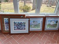 Four framed prints by Cate Mandigo leaned against a window showing detailed folk art scenes.