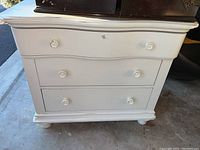 Front view of white painted wooden chest of drawers with three drawers and round knobs.
