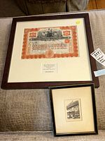 Two framed art pieces shown together: the Marconi stock certificate in a thick dark wood frame with white matting and smaller mid-century etching in a thin black frame.