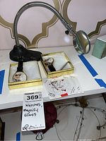 Full view of the two novelty wristwatches displayed in gold boxes along with the goose neck magnifying glass