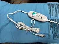 Close-up image of the white Conair branded controller with buttons for moist/dry heat settings and 3 heat levels, connected to blue heating pad.