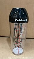 Front view of Cuisinart shaker with black lid and visible whisk inside clear container with red measurement markings.