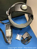 Black LF16B-20 head massager with adjustable band, control knob, and padding. Accessories visible include charger, AA batteries, and storage pouch.