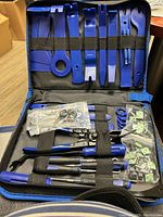 Open tool case showing multiple blue plastic trim removal tools, metal clip pliers, and assorted fasteners organized inside.
